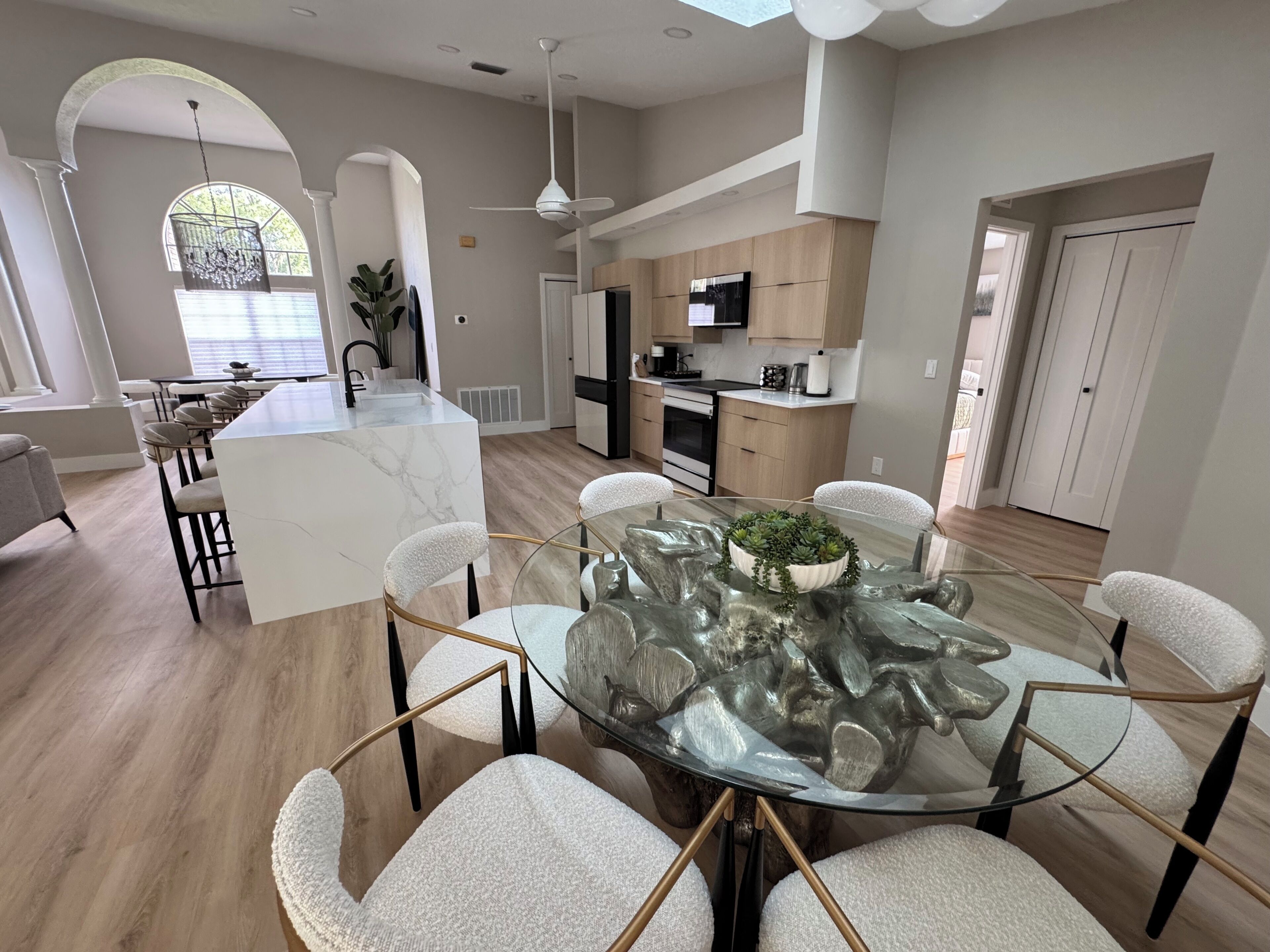 Een moderne keuken met een centraal eiland, een eetgedeelte met een glazen tafel en stoelen, en uitzicht op de woonkamer.