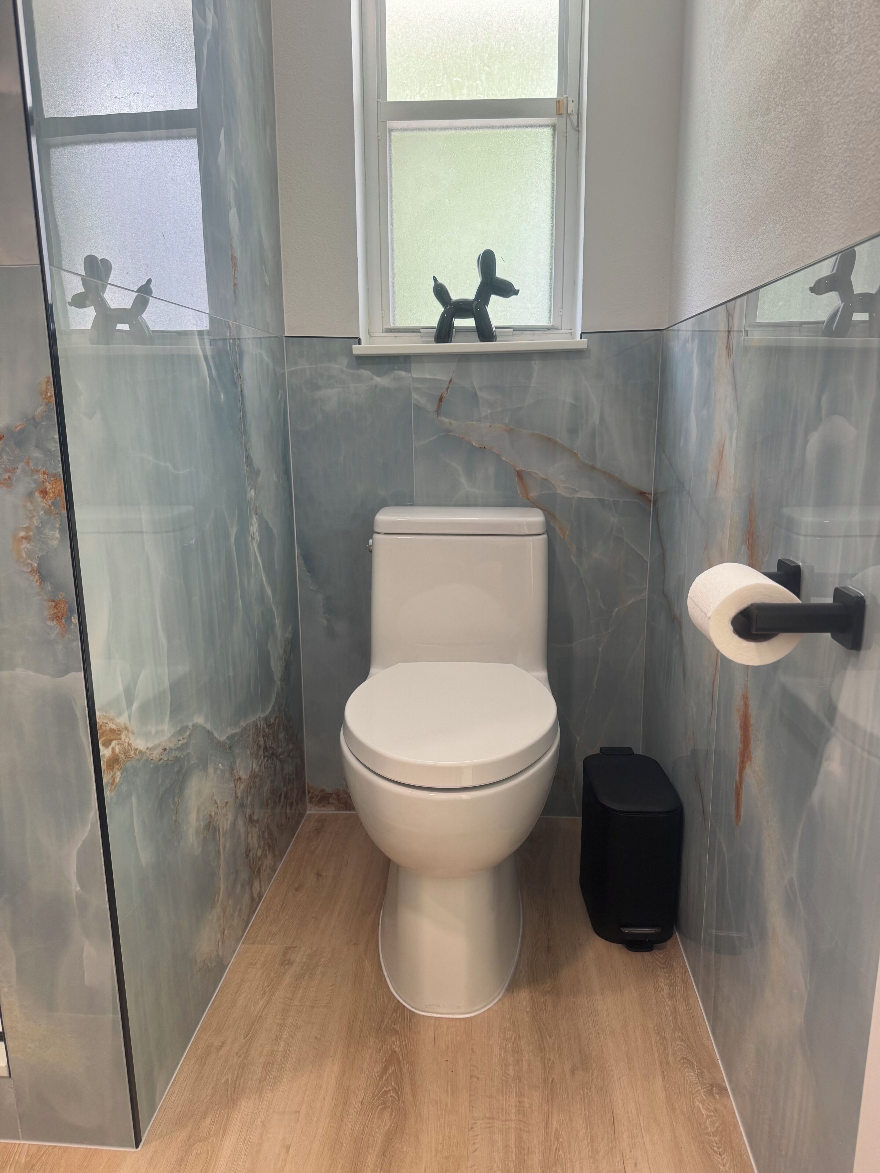 A bathroom with a toilet, a hand dryer, and a window above the toilet.
