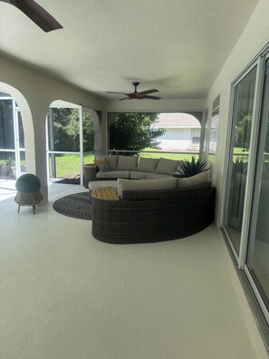 A covered patio with a sectional sofa, a round wicker ottoman, and a ceiling fan. - House on the golf course (Ocala)