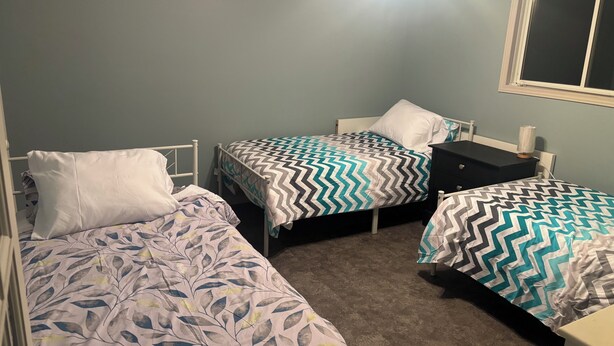 A bedroom with two single beds, a nightstand, a dresser, and a ceiling fan. - Luxury Beach House -Lake Huron : Extra Space at beach & for RV/Travel Trailer. (Central Manitoulin)