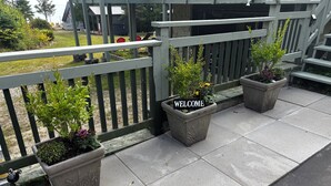 A balcony with a welcome sign, potted plants, and a view of the surrounding area. - Luxury Beach House -Lake Huron : Extra Space at beach & for RV/Travel Trailer. (Central Manitoulin)