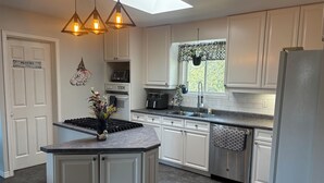 A modern kitchen with white cabinets, a central island, pendant lighting, and a window with a view. - Luxury Beach House -Lake Huron : Extra Space at beach & for RV/Travel Trailer. (Central Manitoulin)