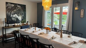 A dining area with a table set for four, chairs, a painting on the wall, and a window with curtains. - Luxury Beach House -Lake Huron : Extra Space at beach & for RV/Travel Trailer. (Central Manitoulin)