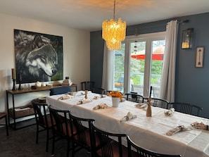 Et spiseområde med et bord dækket til fire personer, stole, et billede på væggen og et vindue med gardiner.
