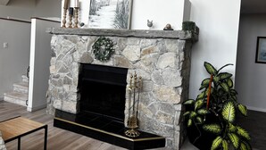 A stone fireplace with a black hearth, a decorative wreath, and a framed painting above it. - Luxury Beach House -Lake Huron : Extra Space at beach & for RV/Travel Trailer. (Central Manitoulin)
