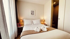 Ein Hotelzimmer mit einem großen Bett, zwei Nachttischlampen, einem gerahmten Bild an der Wand und einer Tür rechts.