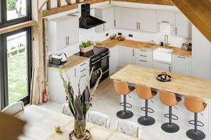 A modern kitchen with white cabinetry, a wooden countertop, and a central island with bar stools. - Barn - Sleeps 10 - Hot Tub - Parking (Reigate)