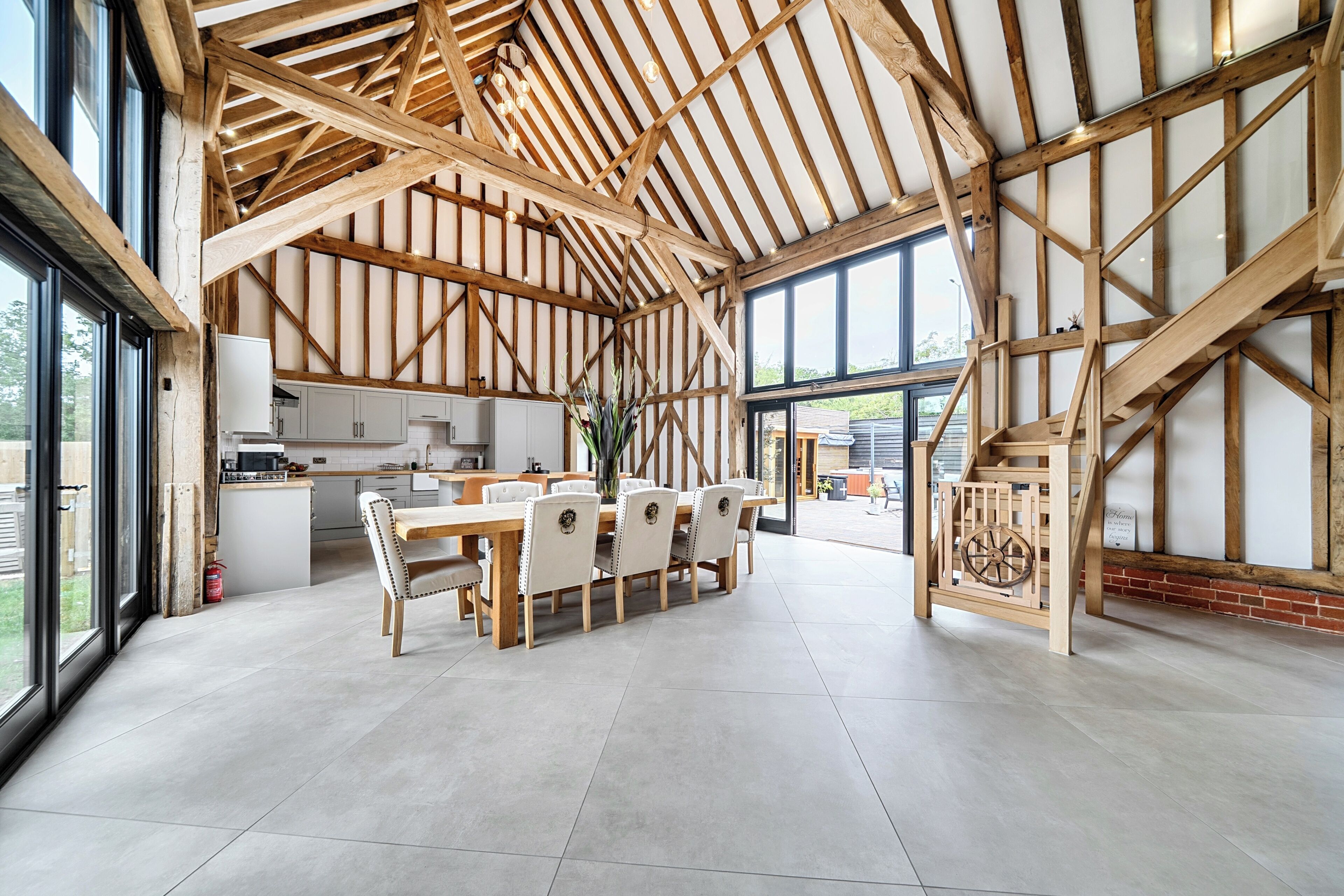 A spacious dining area with a high ceiling and exposed wooden beams, a kitchen adjacent to the dining space, and large windows providing natural light.