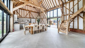 A spacious dining area with a high ceiling and exposed wooden beams, a kitchen adjacent to the dining space, and large windows providing natural light. - Barn - Sleeps 10 - Hot Tub - Parking (Reigate)