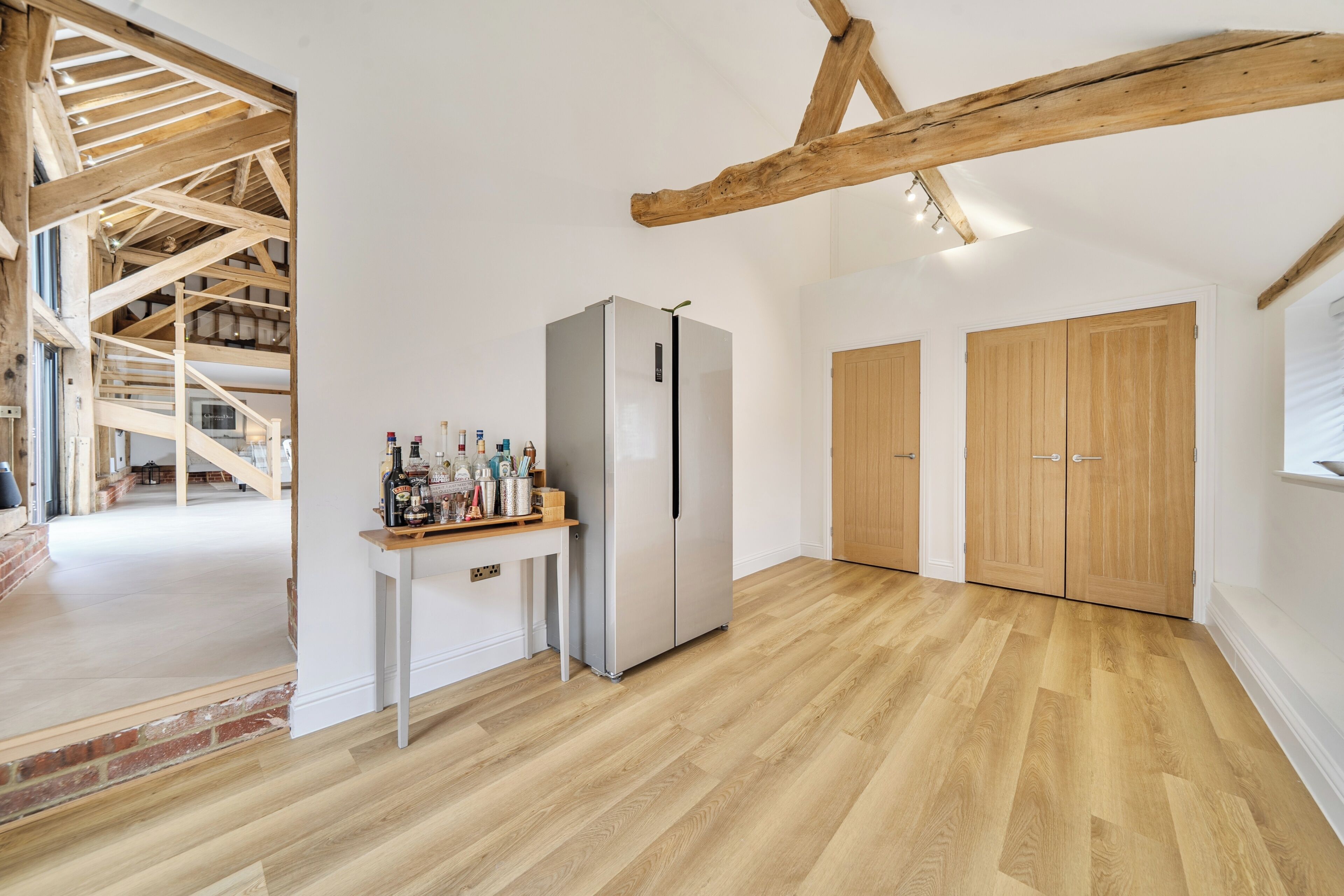A spacious room with a wooden floor, a built-in refrigerator, and a wooden table with bottles.