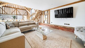 A spacious living room with a large sofa, a glass coffee table, and a TV mounted on the wall. - Barn - Sleeps 10 - Hot Tub - Parking (Reigate)