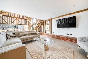 A spacious living room with a large sofa, a glass coffee table, and a TV mounted on the wall. - Barn - Sleeps 10 - Hot Tub - Parking (Reigate)