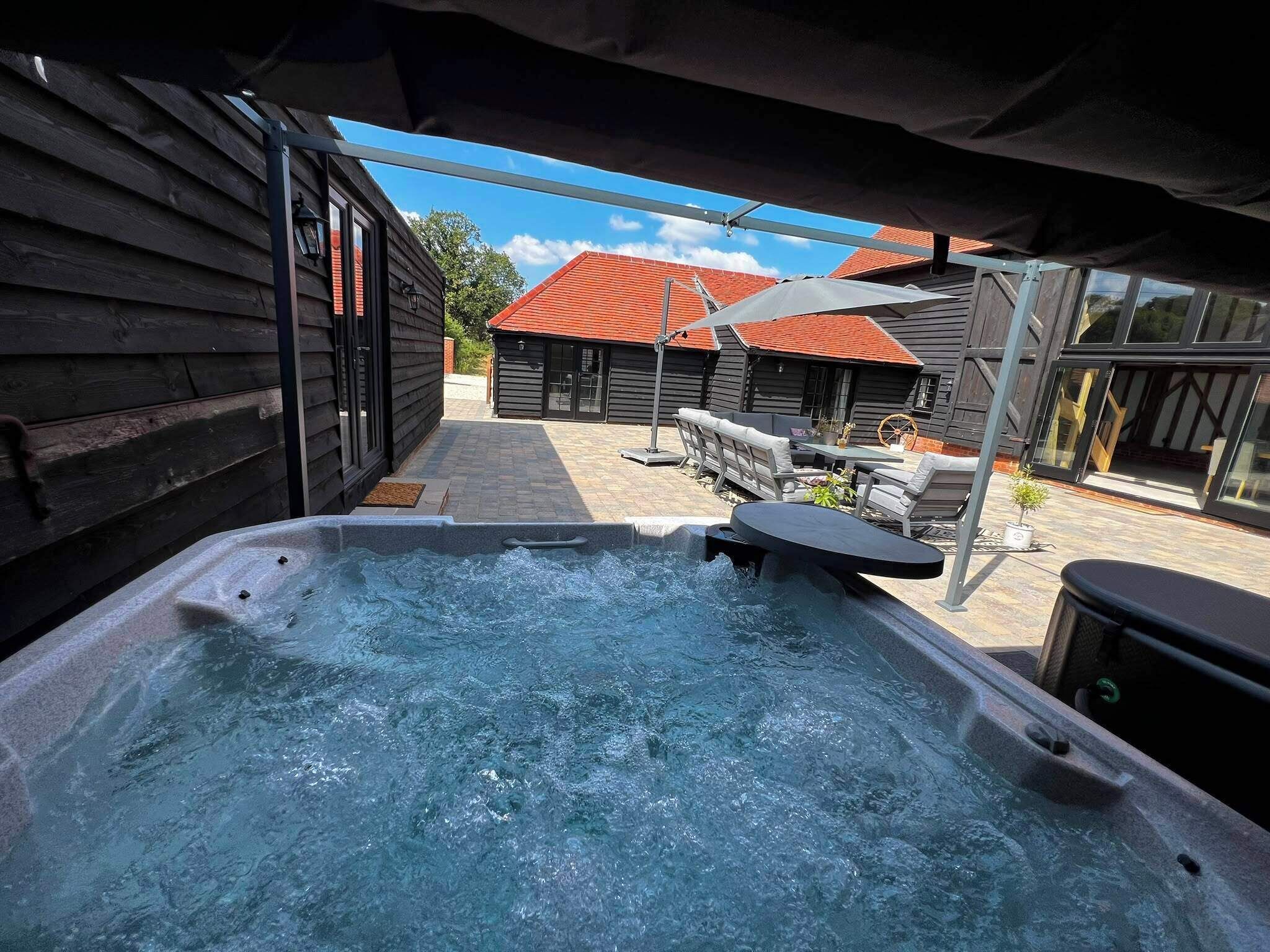 A hot tub area with a view of a wooden building and a red-roofed structure in the background.