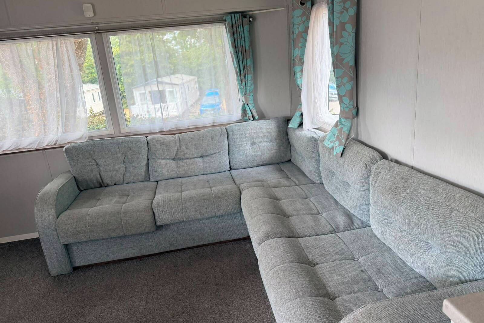 A grey sectional sofa in a room with a window, curtains, and a view of a house outside.