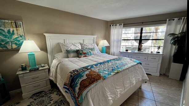Una camera da letto con un letto, comodini, una finestra con tende, un quadro appeso al muro e un tappeto decorato.