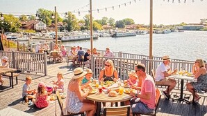 En terrass med bord och stolar, med utsikt över en småbåtshamn med båtar.