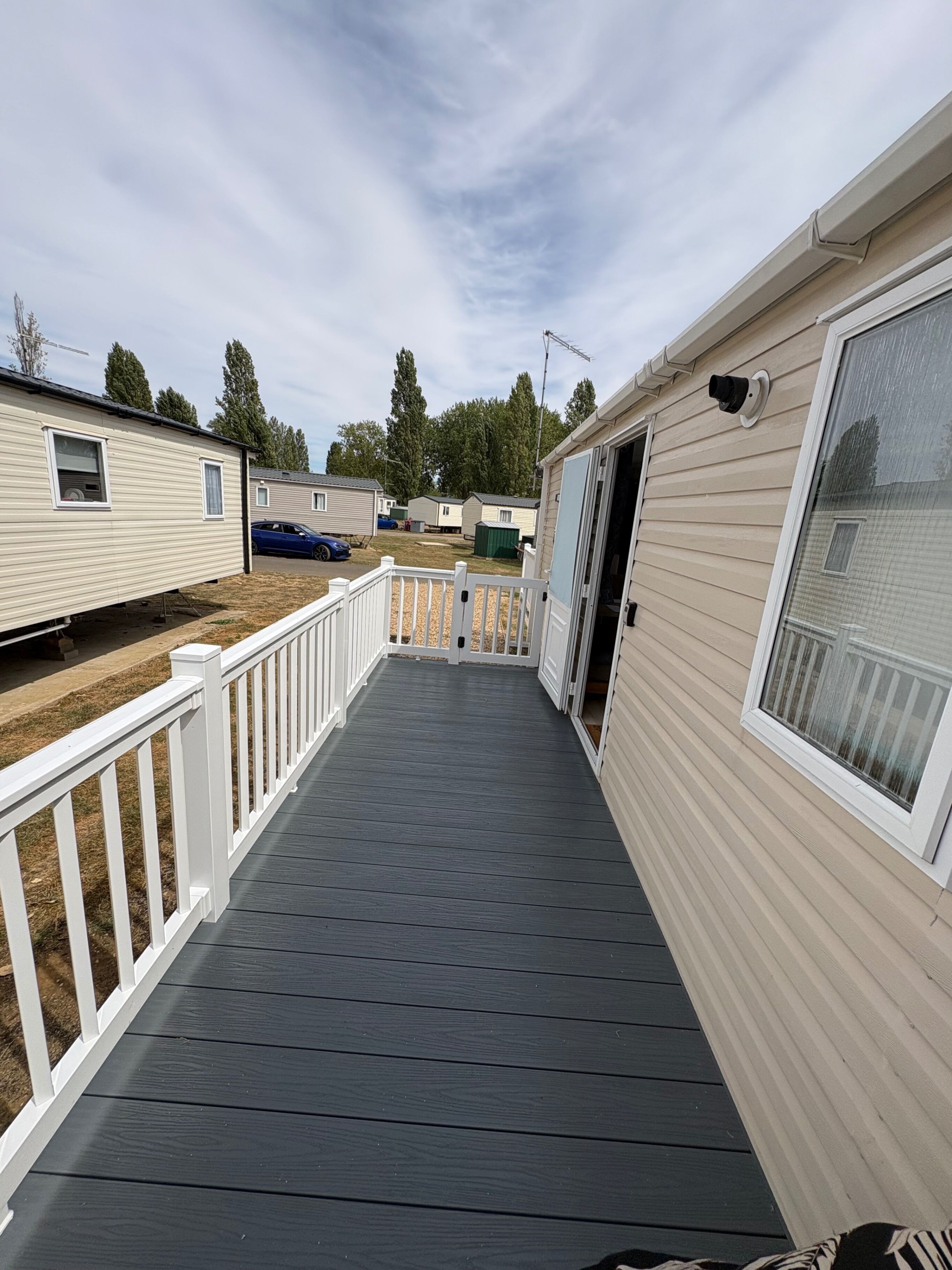 A covered deck area with a white railing, leading to a mobile home with beige siding and a window.