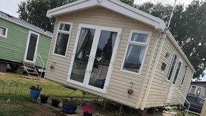 Ett hus på hjul med en veranda framtill, skjutdörrar i glas och ett litet garage som är sammanbyggt med huset.