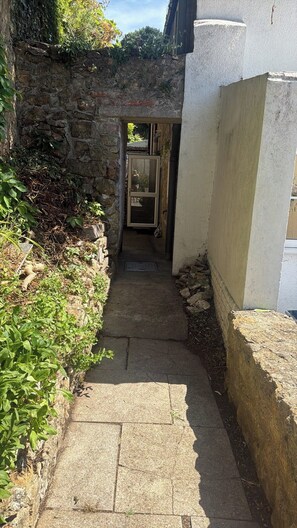 A narrow stone pathway leading to a doorway, flanked by vegetation and a white wall. - Charming Cottage Retreat in Ilminster (Ilminster)