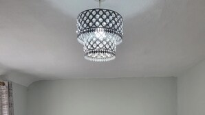 Een net opgemaakt bed met een kussen waarop 'welcome HOME' staat, een decoratieve kroonluchter en twee nachtkastjes met lampen.