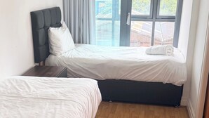 Un dormitorio con dos camas, ventanas amplias y vistas a edificios.