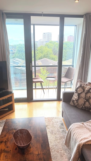 A spacious living area with a large sliding glass door leading to an outdoor balcony, a sofa, a coffee table, and a television. - Luxury Central London Apartment Paddington (London)