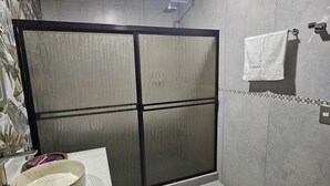 A bathroom with a glass shower enclosure, a sink with a marble basin, and a towel hanging on the wall. - Divina Naturaleza (Fortuna)