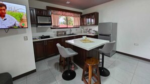 A modern kitchen with a dining area, a TV mounted on the wall, and a refrigerator. - Divina Naturaleza (Fortuna)