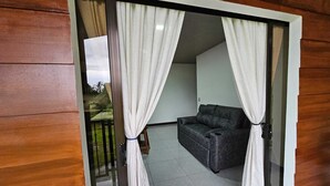 A balcony with a sliding door, a dark sofa, and a view of a garden. - Divina Naturaleza (Fortuna)