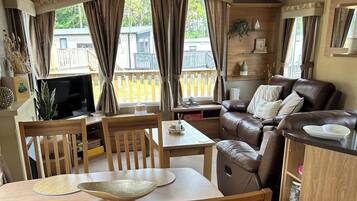 A cozy living room with a brown leather sofa, wooden dining table, and chairs.