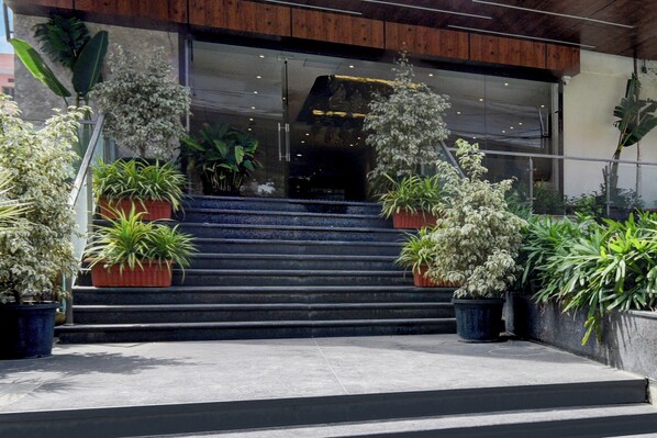Entrada de um edifício com escadaria, plantas em vasos e teto de madeira.