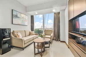 Ein modernes Wohnzimmer mit Sofa, Sessel, Couchtisch, Fernseher und einem Gemälde an der Wand.