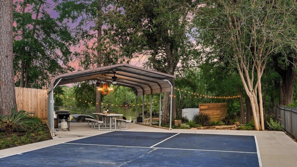 A covered outdoor seating area with tables and chairs, a barbecue grill, and string lights.