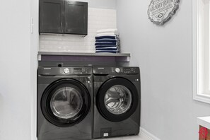 A laundry room with two Samsung front-loading washers, a white tiled wall, and a laundry sign.