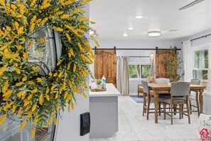A modern kitchen with a dining area, featuring a large window, wooden cabinets, and a central island with a water dispenser.