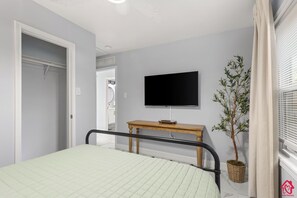 A bedroom with a bed, a television mounted on the wall, a wooden bedside table, and a potted plant.