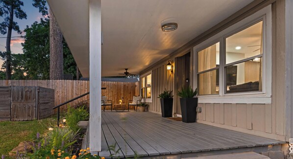 A covered porch with a wooden deck, a seating area with chairs, and a potted plant.