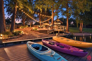 A wooden deck with kayaks, a covered outdoor seating area, and string lights.