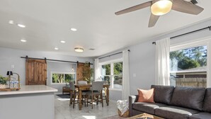 A modern living room with a glass coffee table, a dark leather sofa, and a dining area with a wooden table and chairs.