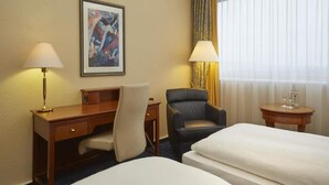 A hotel room with a desk, two chairs, a bed, a painting on the wall, and a window with curtains. - 3 Person Holiday Park Home in Kassel (Kassel)