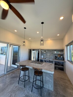 A modern kitchen with a central island, bar stools, recessed lighting, and a view through the glass door. - Casa El Viento: Modern 3-Bedroom Desert & Sea Retreat in El Sargento (El Sargento)