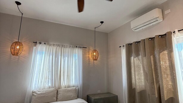 A bedroom with a bed, ceiling fan, air conditioning unit, bedside lamps, and curtains. - Casa El Viento: Modern 3-Bedroom Desert & Sea Retreat in El Sargento (El Sargento)