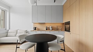 A modern kitchen with grey cabinets, a wooden countertop, and a round table with chairs. - Zamojska Skyline View Apartment (Lublin)