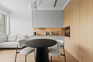 A modern kitchen with grey cabinets, a wooden countertop, and a round table with chairs. - Zamojska Skyline View Apartment (Lublin)