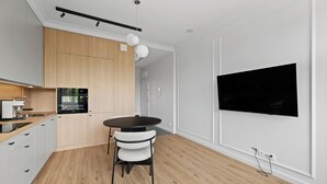 A modern kitchen with wooden cabinets, a black countertop, a round dining table with chairs, and a mounted flat-screen TV. - Zamojska Skyline View Apartment (Lublin)
