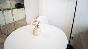 Ein weißer Tisch mit einer Vase, in der eine einzelne Rose steht, ein weißer Stuhl und im Hintergrund eine Küchenzeile.