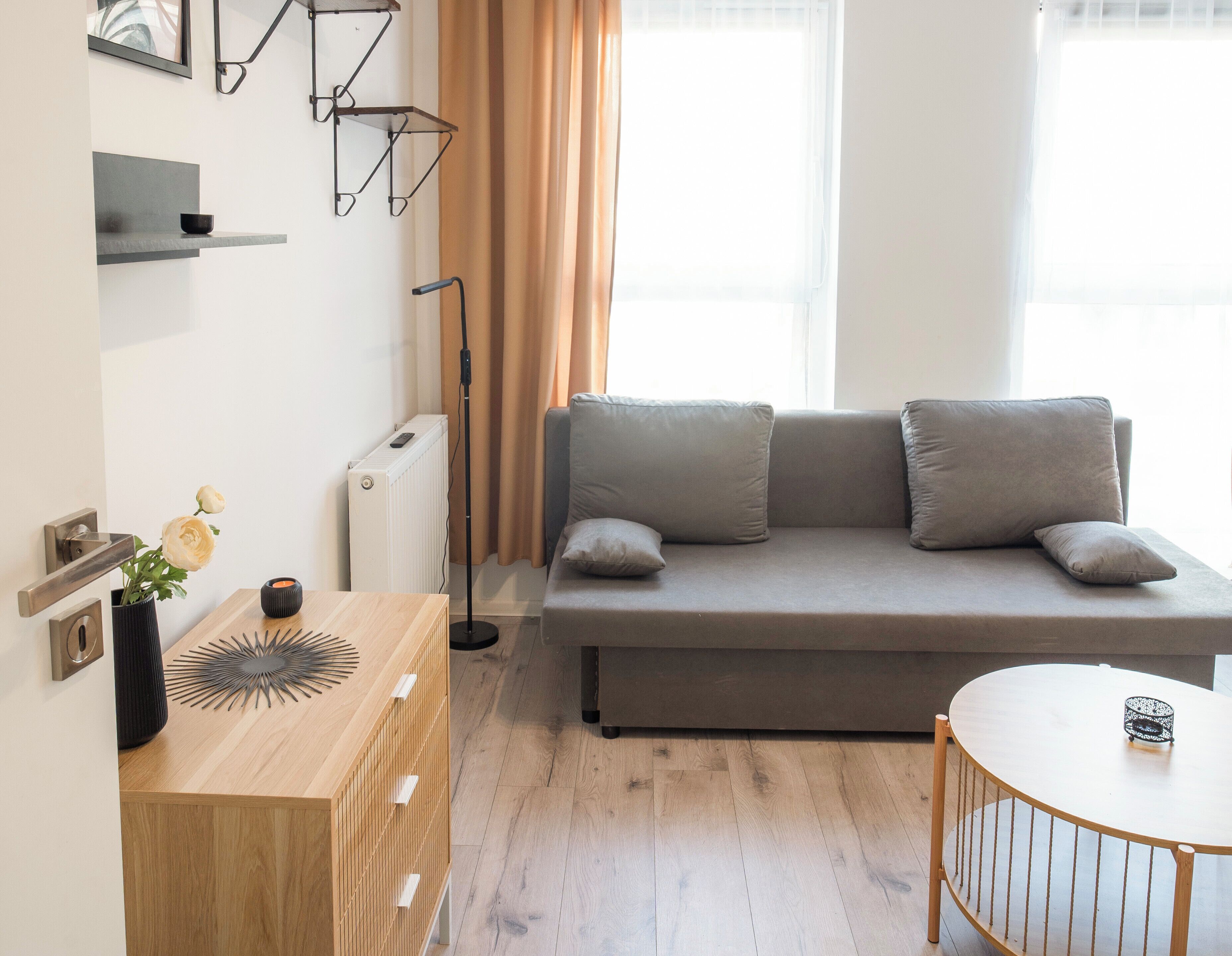 En moderne stue med en sofa, et træ sidebord, en gulvlampe og et rundt bord.