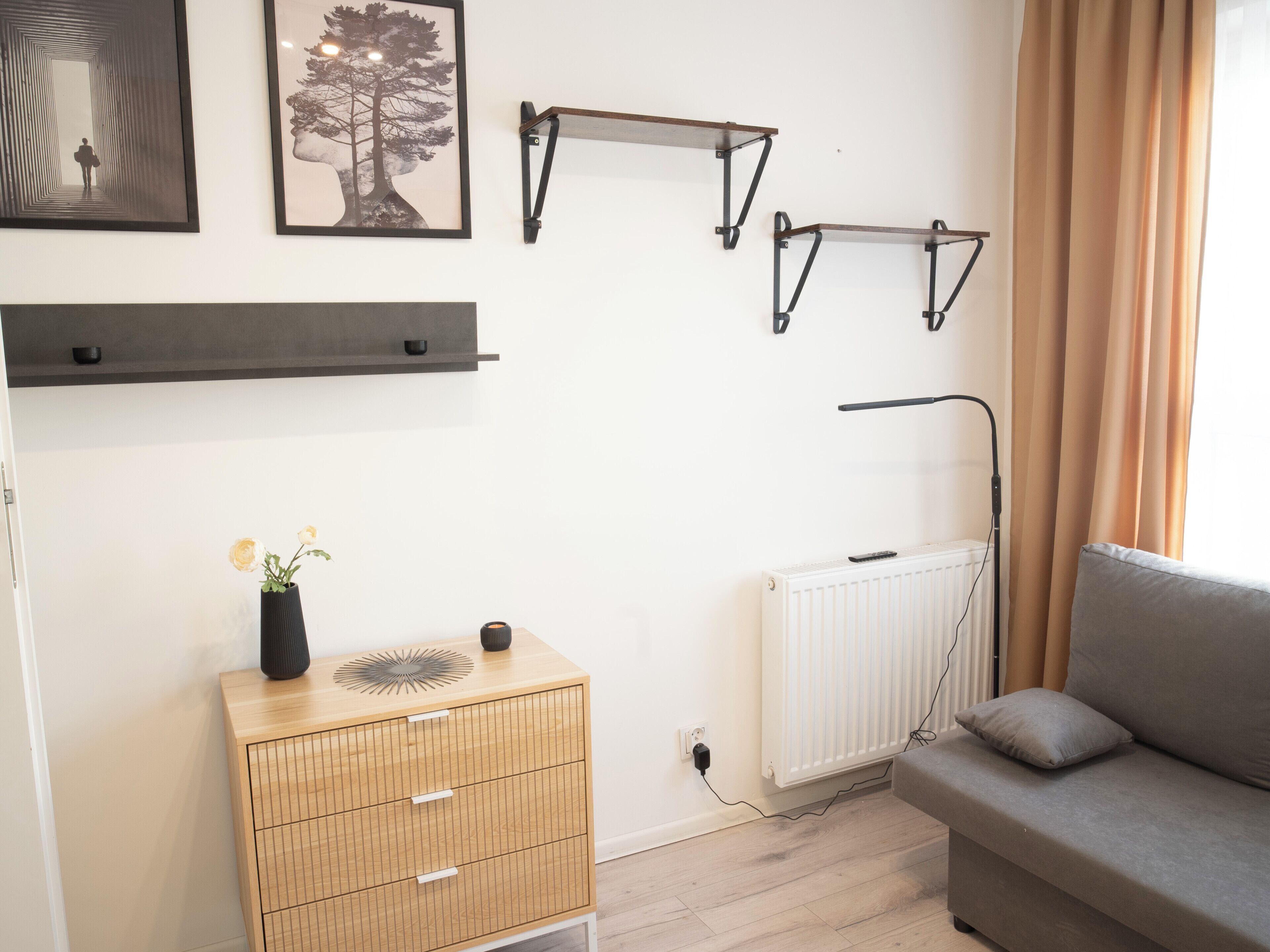 Une pièce comprenant un canapé, un radiateur, un meuble en bois orné d’un vase et des étagères fixées au mur.