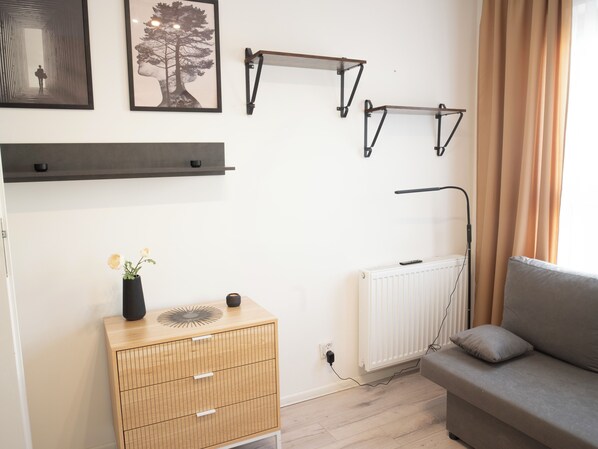 Una habitación con sofá, radiador, aparador de madera con un florero y estantes en la pared.