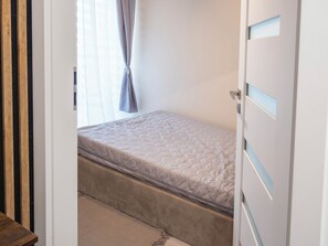 Un dormitorio con cama, puerta y ventana con cortinas.